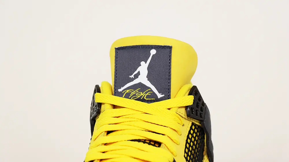A front view of the tongue on the Jordan 4 Retro ‘Lightning’ (2021), featuring yellow suede material and a black fabric logo patch.