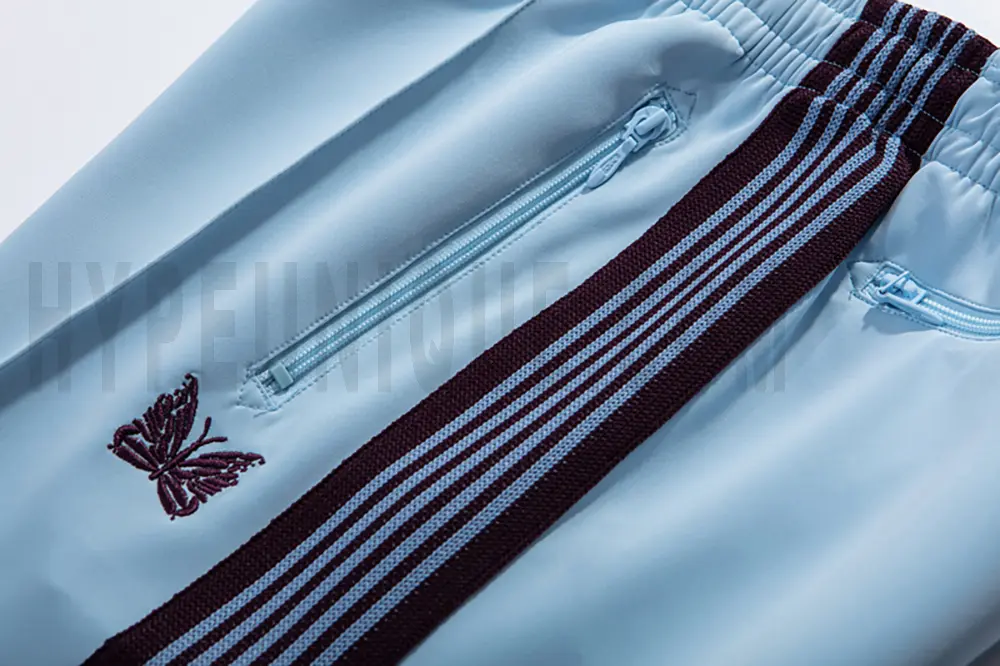 Close-up detail of the track pants pocket and delicate butterfly embroidery.