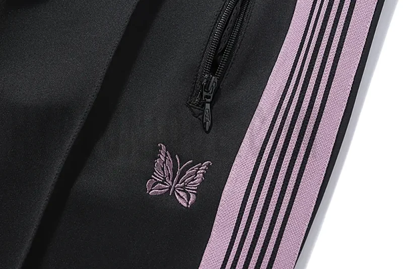 Close-up detail of the track pants pocket and delicate butterfly embroidery.
