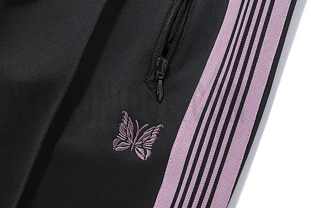 Close-up detail of the track pants pocket and delicate butterfly embroidery.