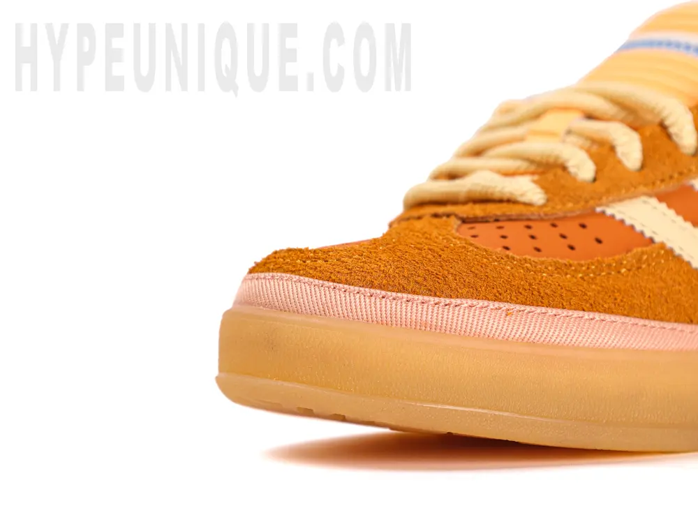 A close-up of the toe box of the left shoe of the Bad Bunny x Gazelle Indoor 'Santurce' and hypeuniqeu branding and photos, showing the rubber outsole and orange toe box.