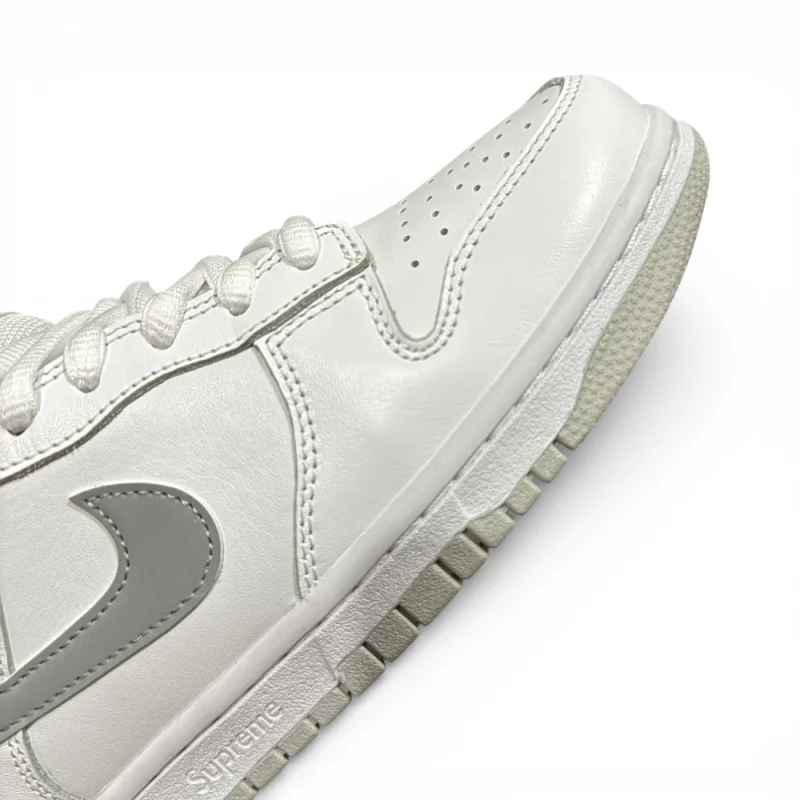 Angled close-up of toe area highlighting smooth white leather, perforations, and midsole texture