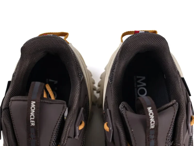 Top view of a pair of brown athletic sneakers with yellow pull tabs and black mesh lining. The insoles display a logo, and stretchy laces are visible. The shoes are placed closely, facing outward.