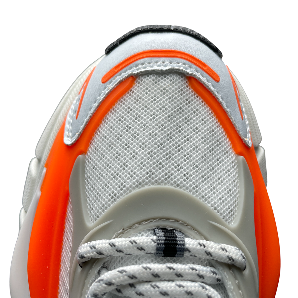 Close-up of a sneaker's mesh upper with orange and gray accents, highlighting textured fabric, layered design, and dynamic angles.