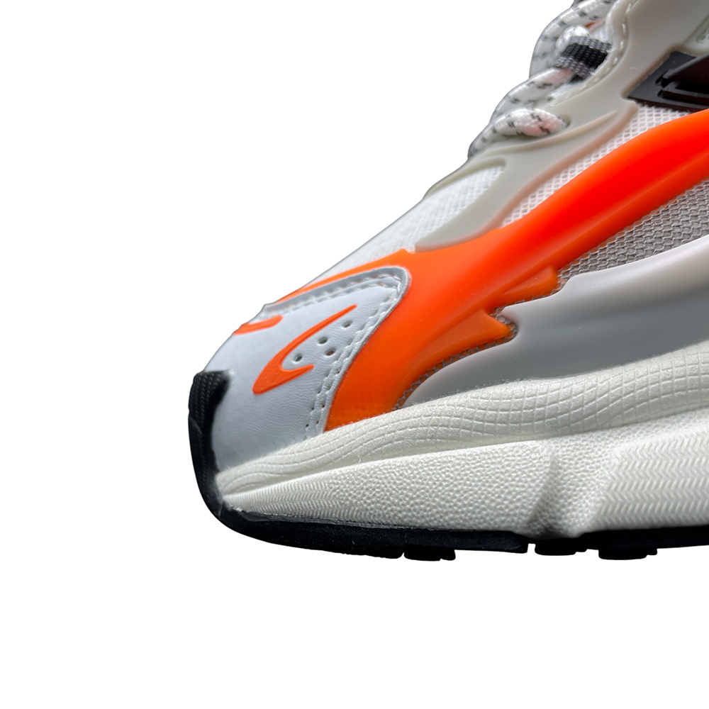 Hand holding a sneaker showing back view; white mesh and leather with vibrant orange accents, highlighting textured materials and curves.
