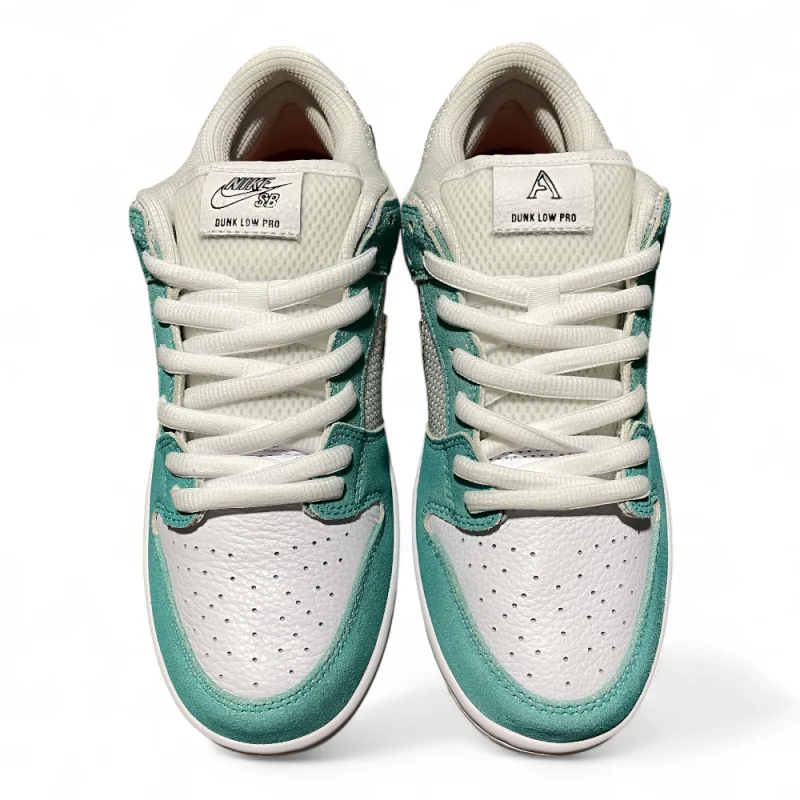 Close-up of a sneaker's tongue in white mesh, with teal suede accents and white laces crossing diagonally.