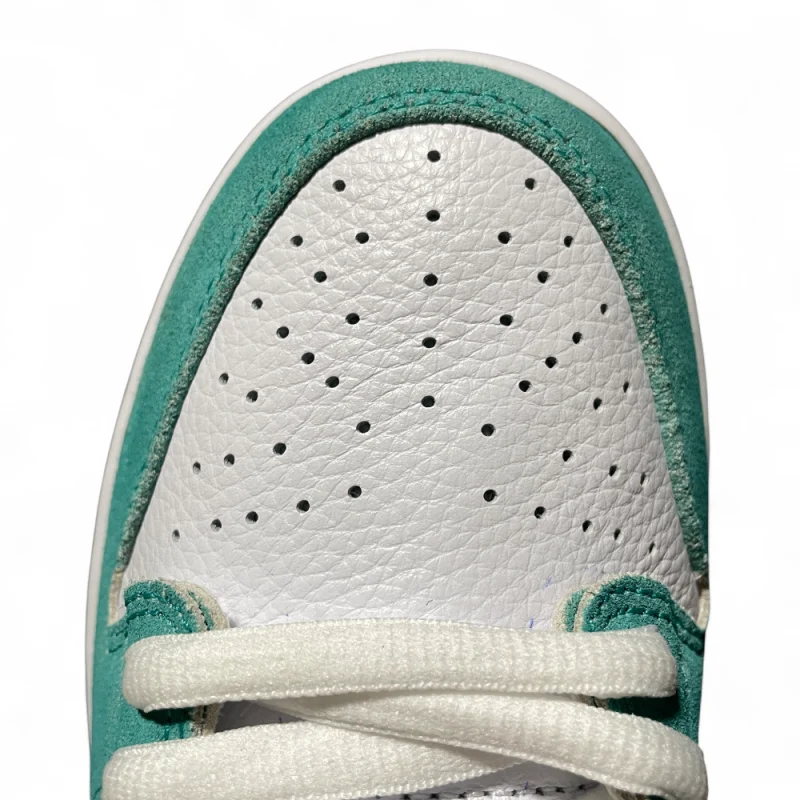 Close-up of a sneaker toe: white leather with perforations, teal suede trim, and white laces crisscrossing at an angle.