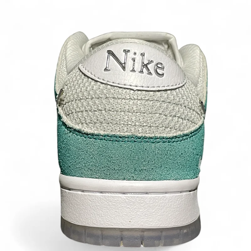 Close-up of a sneaker heel, showcasing textured teal suede, white mesh, and leather with metallic text against a white background.