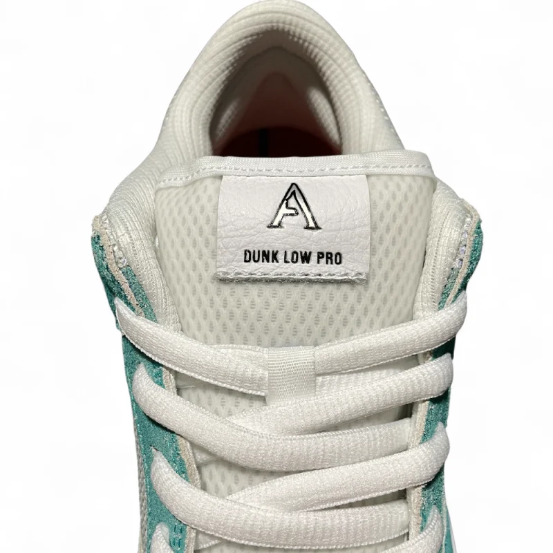 Close-up of a sneaker's tongue with white mesh material, teal suede accents, and flat white laces crossing diagonally.