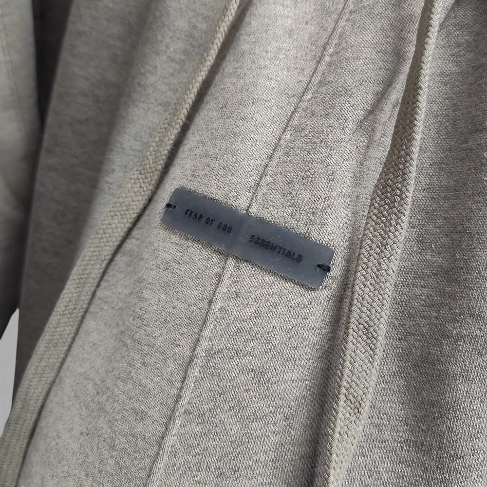 Gray fabric hoodie with a branded black label, showcasing stitching detail.