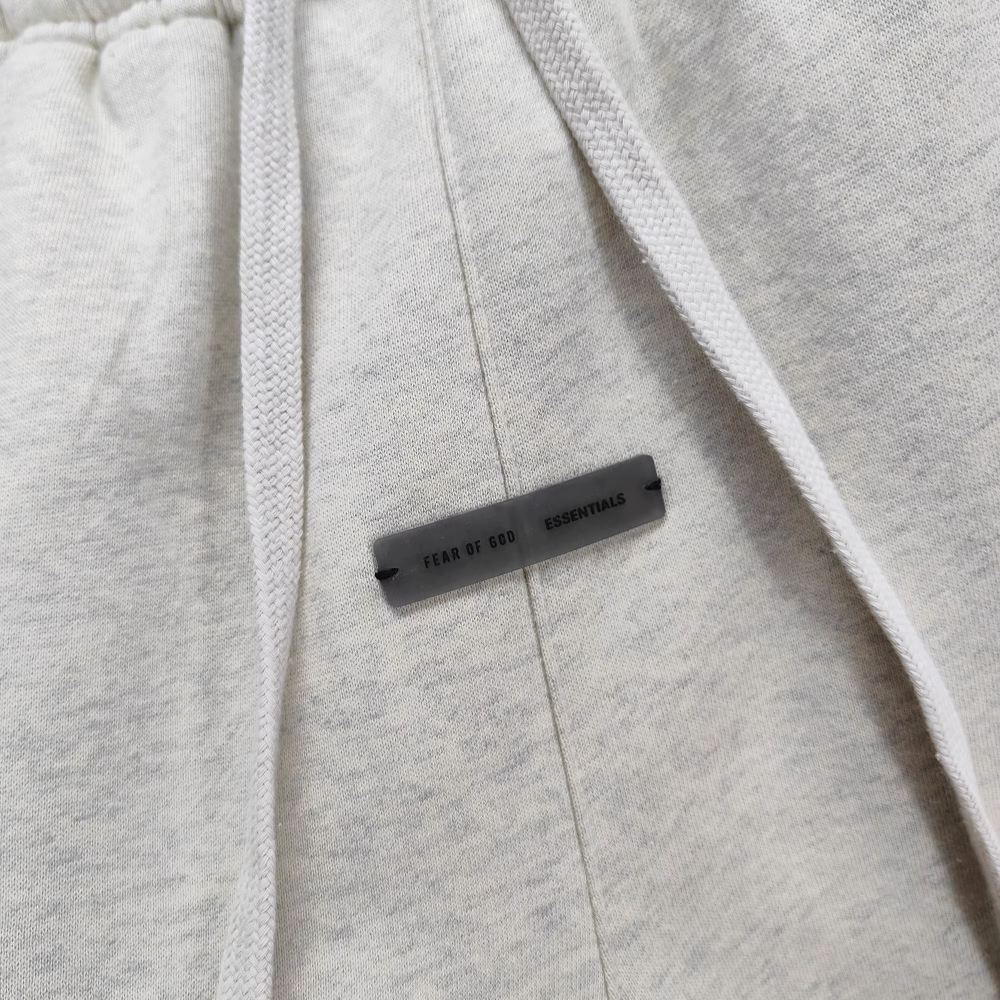 Close-up of light grey fabric sweatpants with drawstrings and a branded rubber tag.