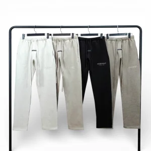 Four pairs of sweatpants in beige and black, cotton material, displayed on hangers.