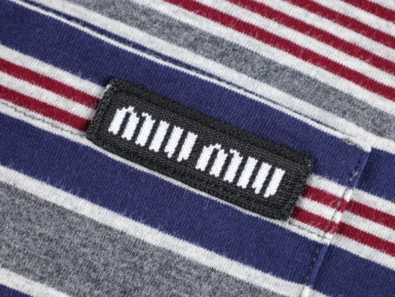 Striped fabric in red, gray, and navy with a black rectangular label featuring white text, stitched diagonally.