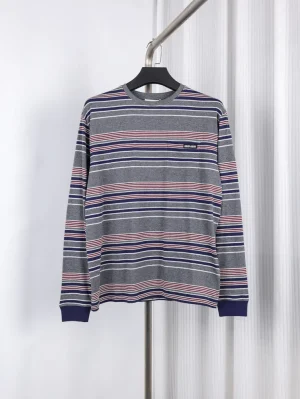 Gray long-sleeve shirt with horizontal blue, red, and white stripes, hanging on a black hanger against a white background.
