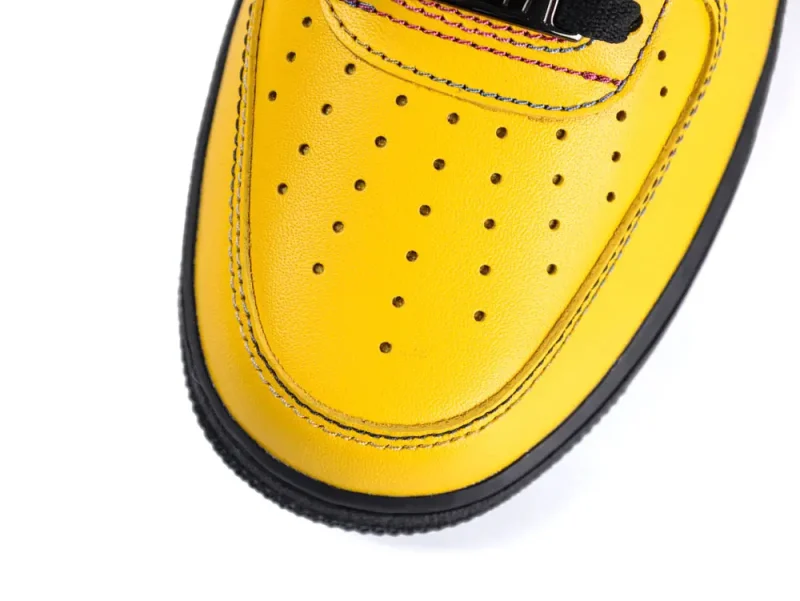 Yellow leather shoe toe with perforations and black stitching detail, close-up view.