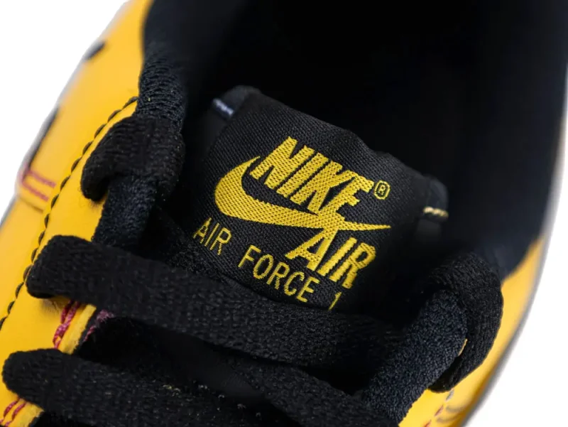 Black and yellow fabric sneaker tongue with black laces, featuring bold logo design.