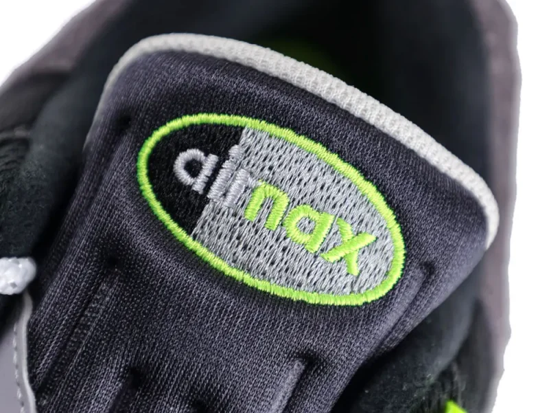 Black and gray fabric sneaker tongue with green and white embroidered text.