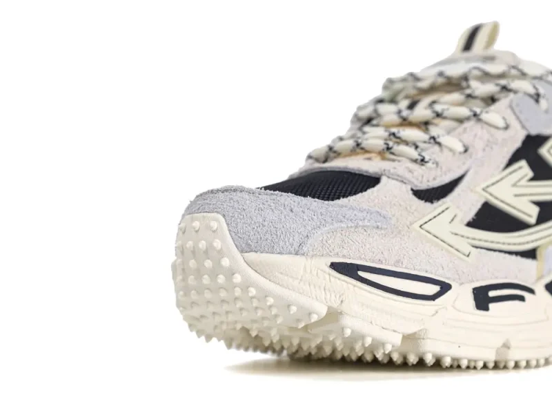 Beige and black suede sneaker with textured sole and patterned laces, close-up view.