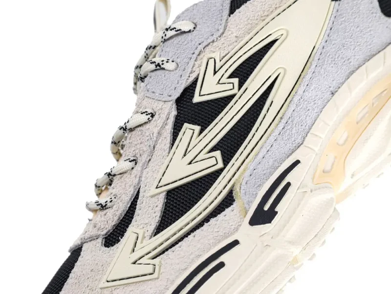 Beige and black sneaker with suede and mesh materials, featuring arrow designs and laces.