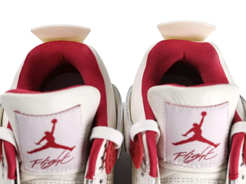 Close-up of white leather sneakers with red fabric lining and branded tongue details.