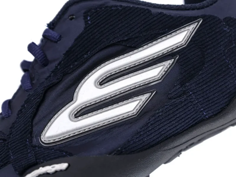 Navy blue sneaker with fabric upper and white stitched logo design on the side.