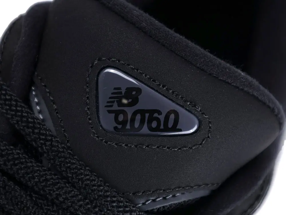 Black synthetic shoe tongue featuring a plastic logo accent with raised text.