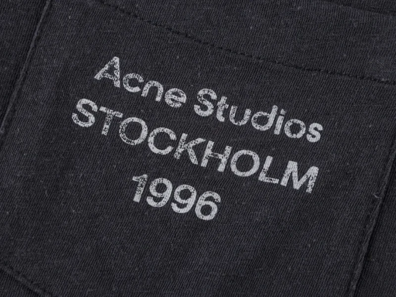 Close-up of black fabric with white printed text, featuring pocket detail.