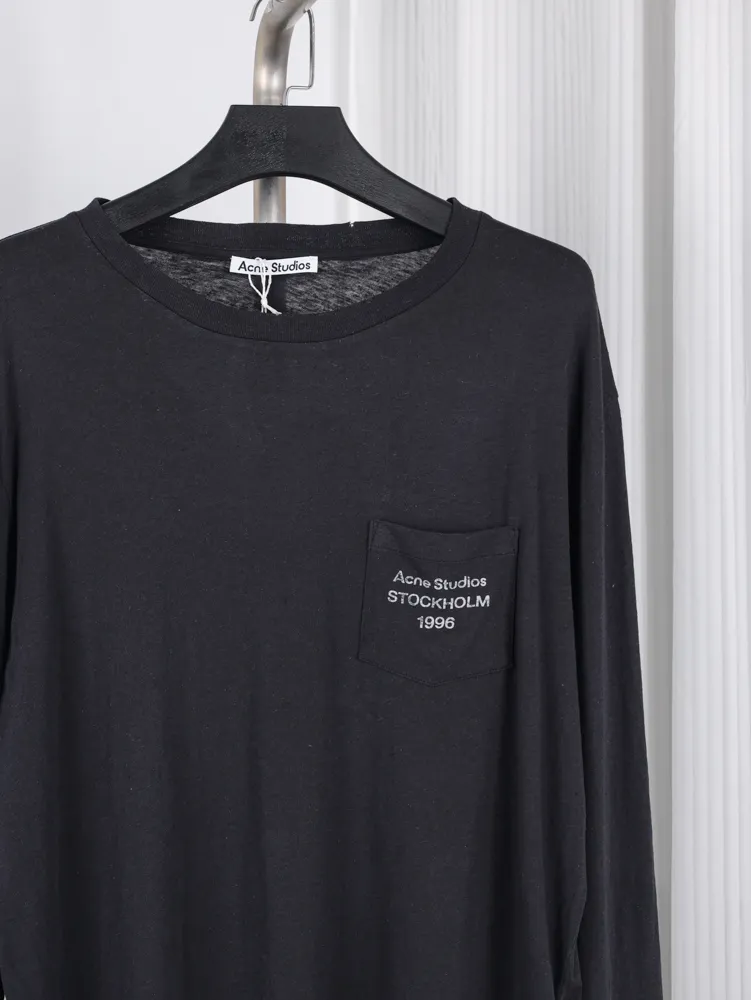 Black cotton long-sleeve shirt featuring a chest pocket with embroidered text.