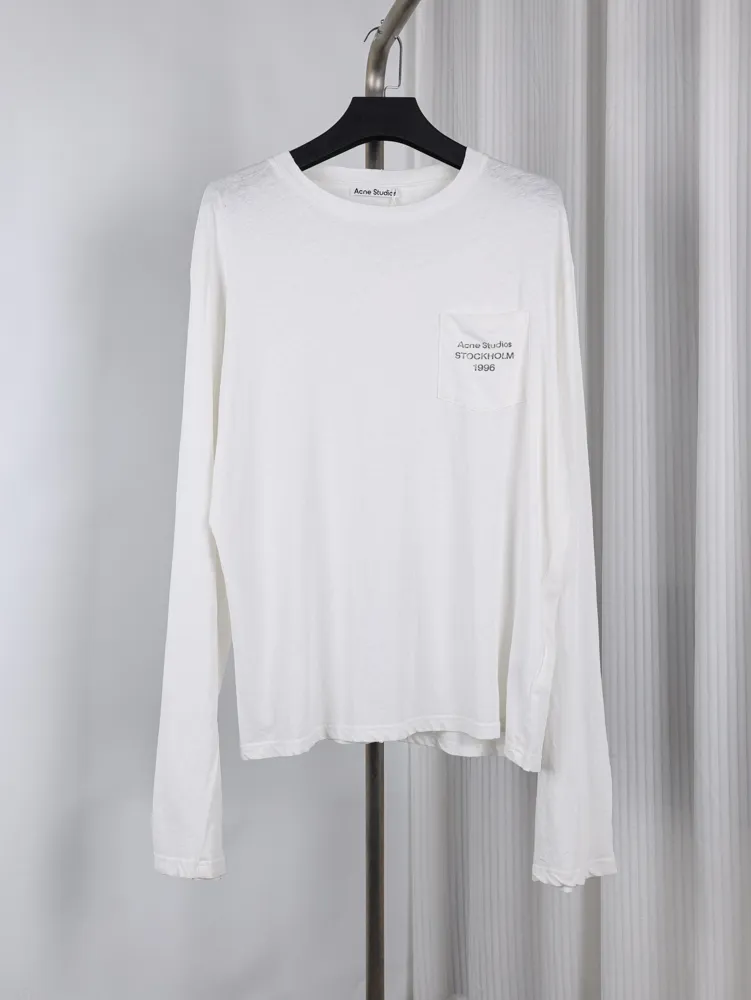 White cotton long-sleeve shirt with a chest pocket, hanging on a black hanger.