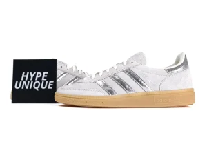 White suede sneakers with silver metallic stripes and a tan rubber sole.