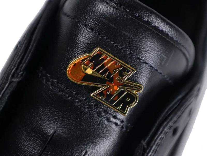 Black leather shoe with gold and orange logo on upper part.