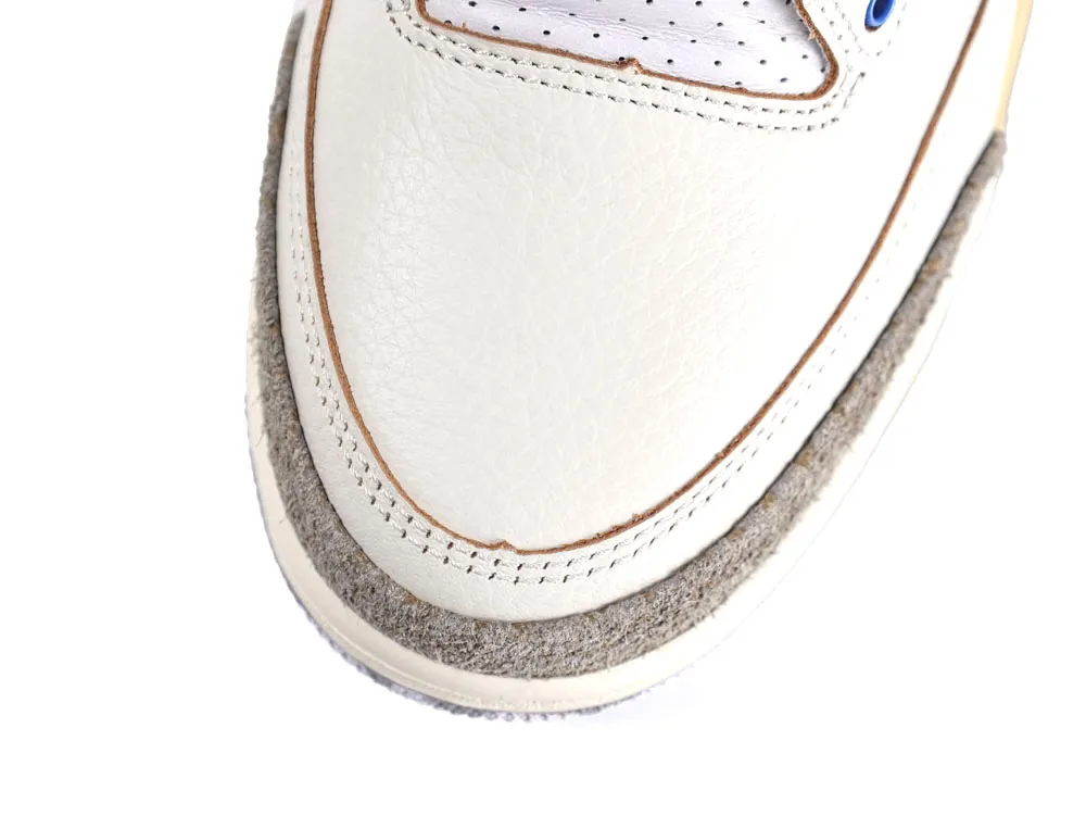 Close-up of a white leather sneaker's toe, featuring gray suede trim.