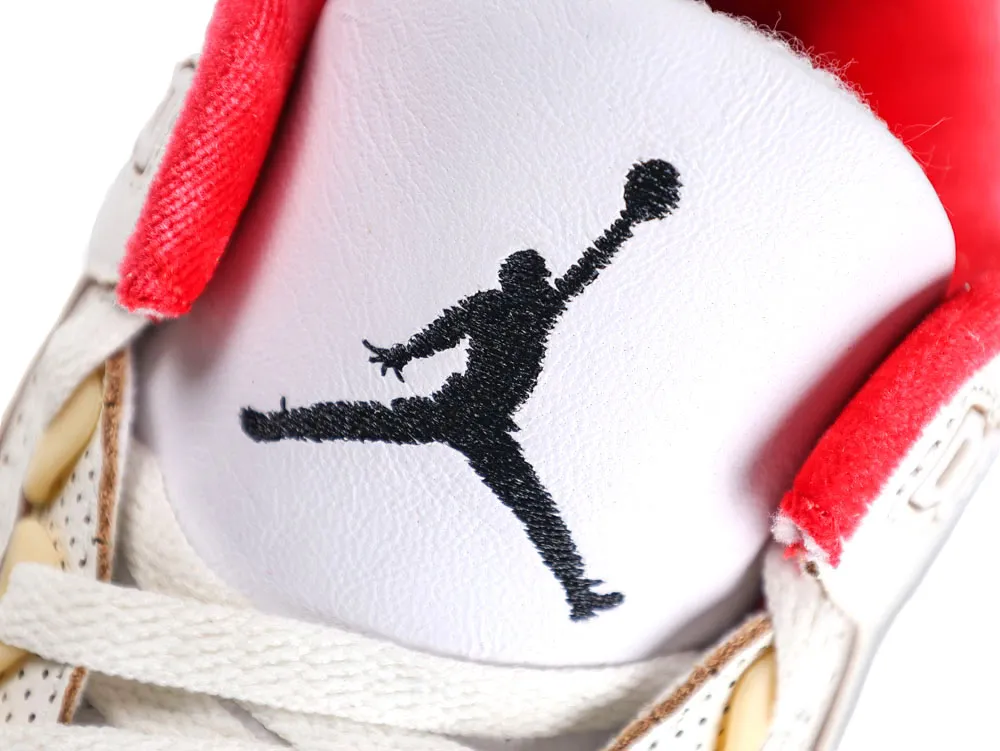 Close-up of white leather sneaker tongue with red fabric accents and black logo.
