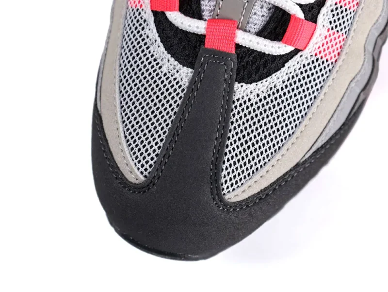 Close-up of a gray mesh sneaker toe with black suede and red accents.