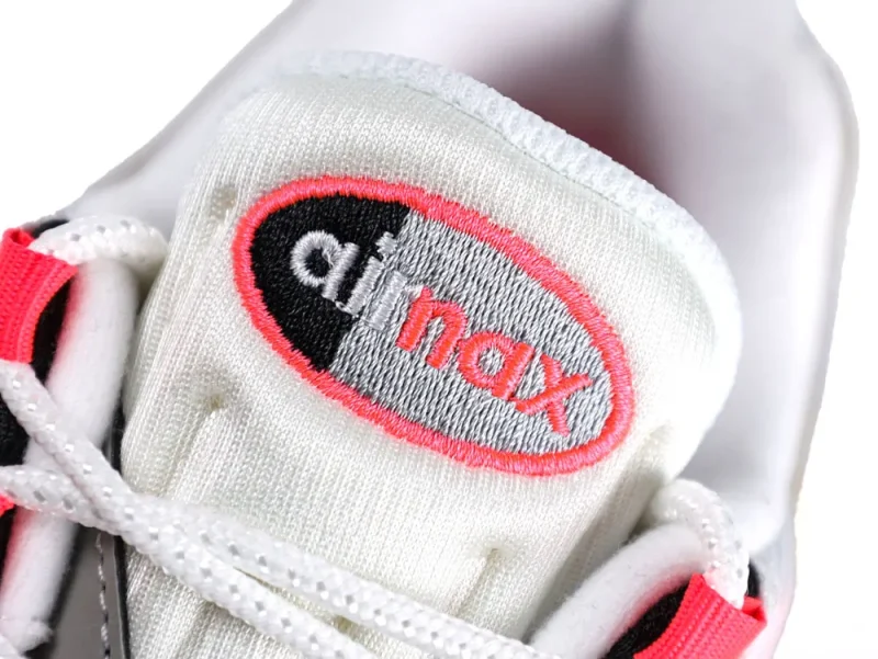 Close-up of white fabric shoe tongue with gray and red embroidered logo.