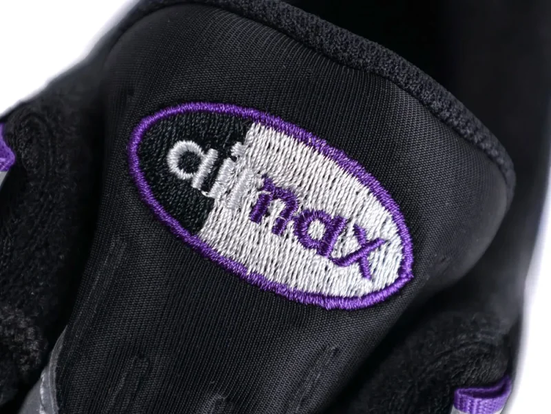 Black fabric shoe tongue with purple embroidered logo and white details.