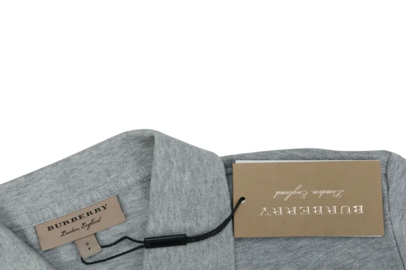 Grey fabric garment with a collar and beige tags attached, featuring brand labels.