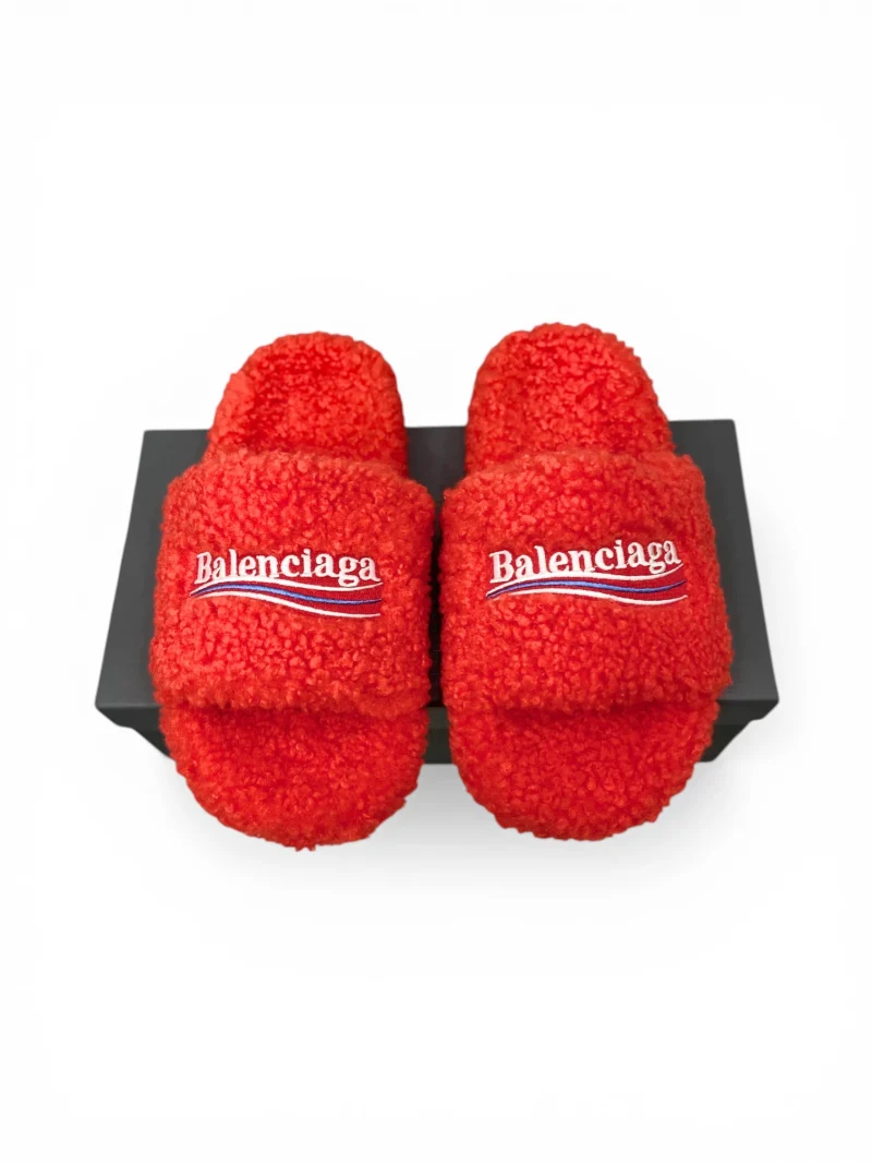 Red fluffy slippers with logo on strap, displayed on a black box.