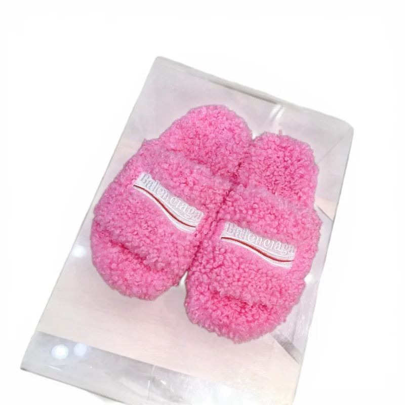 White fluffy slippers with embroidered logo on strap, made from soft material.