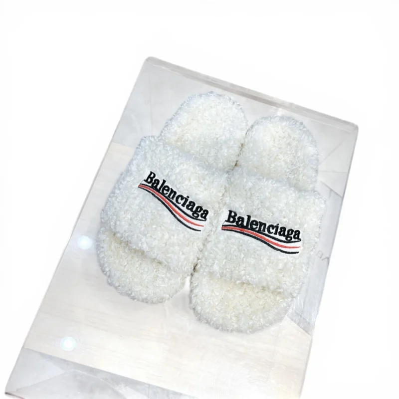 White fluffy slippers with embroidered logo on strap, made from soft material.