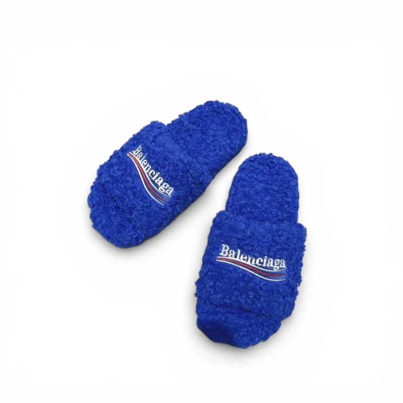 Blue fuzzy slippers with embroidered logo on top, made from soft material.