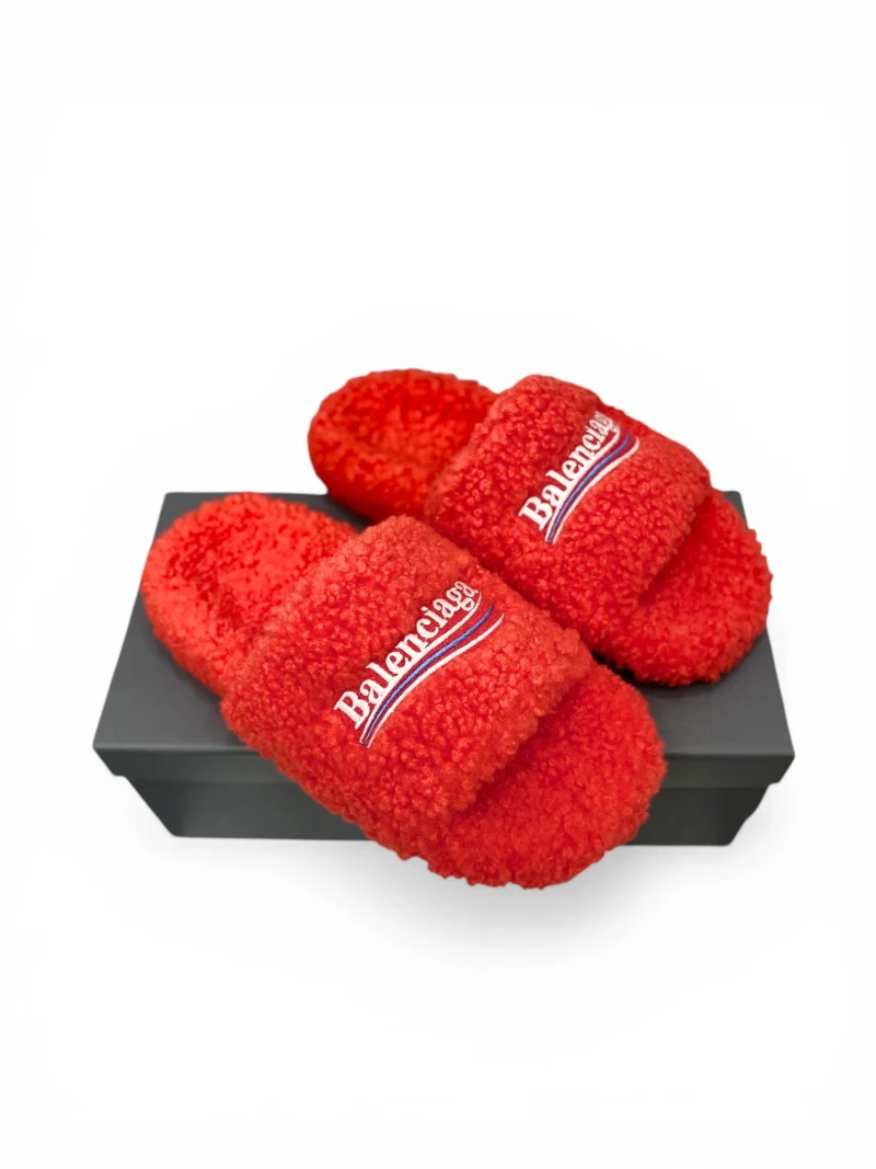 Red fleece slippers with logo embroidery, resting on a black box.