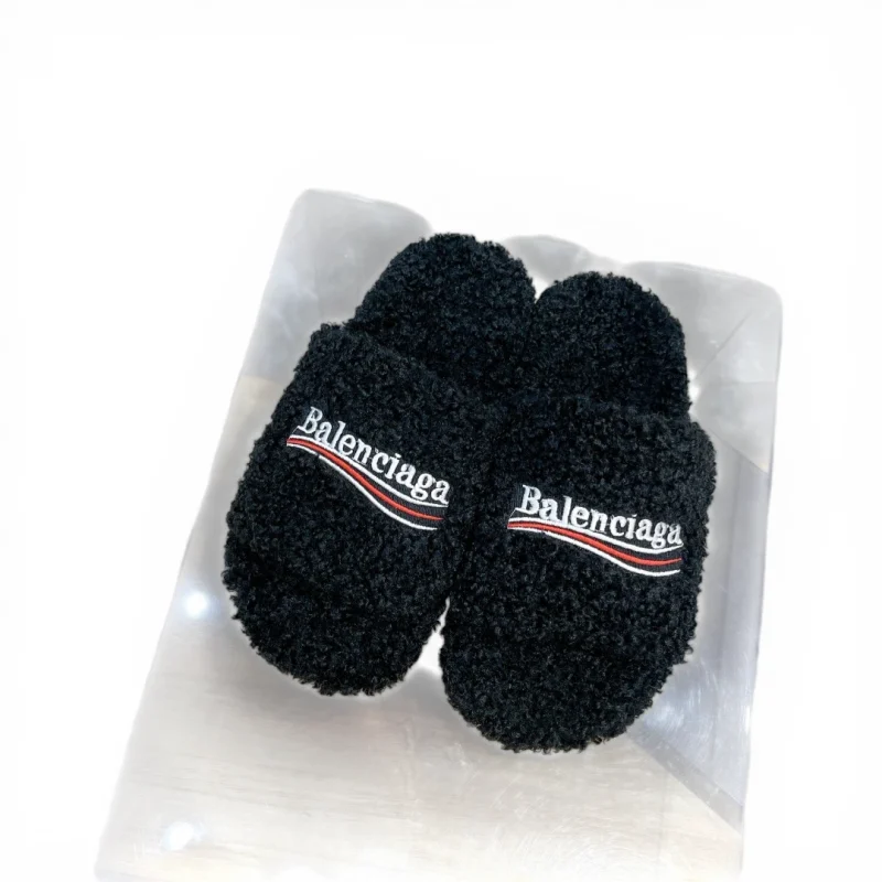 Black fleece slippers with embroidered text on top, displayed on a wooden surface.