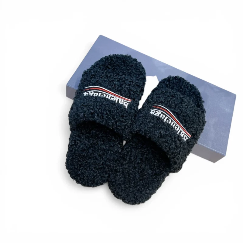 Black fuzzy slippers with embroidered logo, placed on a blue box.