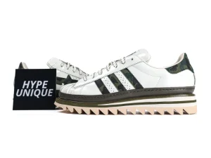 White leather sneaker with green camouflage accents and jagged sole.