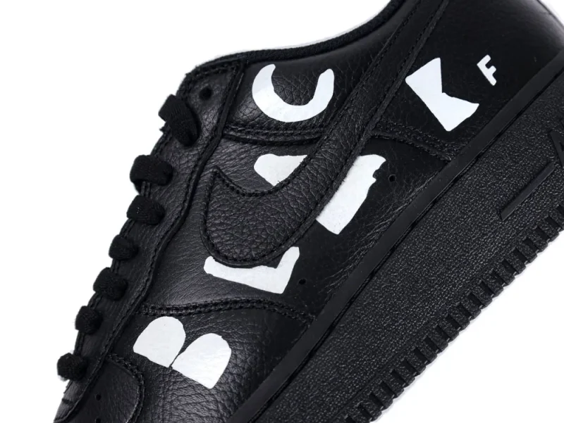 Black leather sneaker with bold white letters and black laces, close-up view.