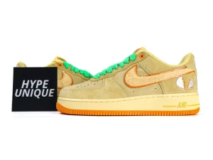 Tan suede sneaker with orange accents and green laces, featuring an embossed logo.