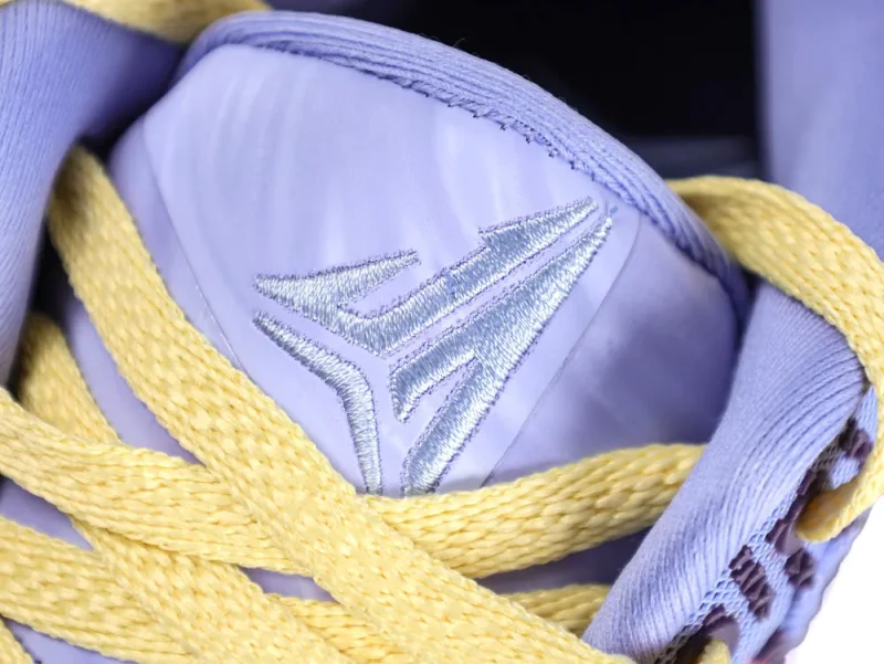 Purple fabric sneaker tongue with yellow laces and embroidered silver logo.