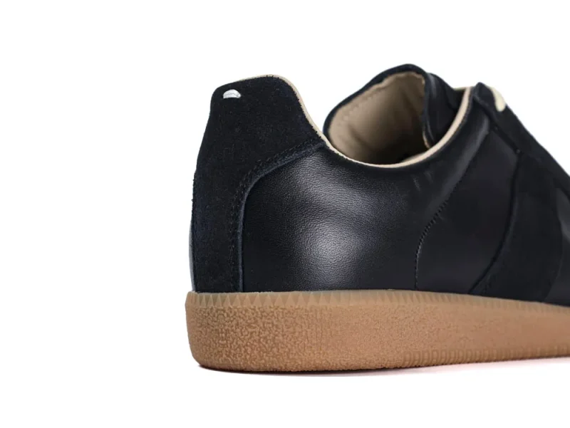 Black leather shoe with suede detail and tan rubber sole.