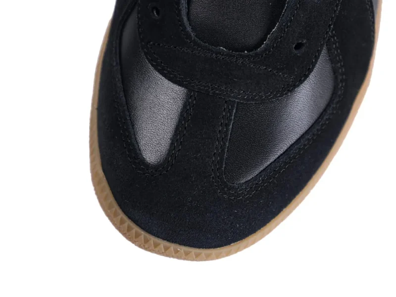 Black suede and leather sneaker with a brown rubber sole close-up.
